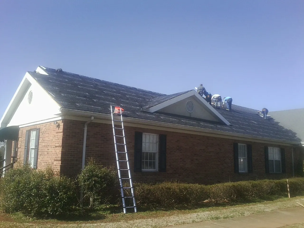 Crew tearing shingles off a brick ranch roof with a ladder set — Emergency Roof Repair work by our crew in Bear Creek