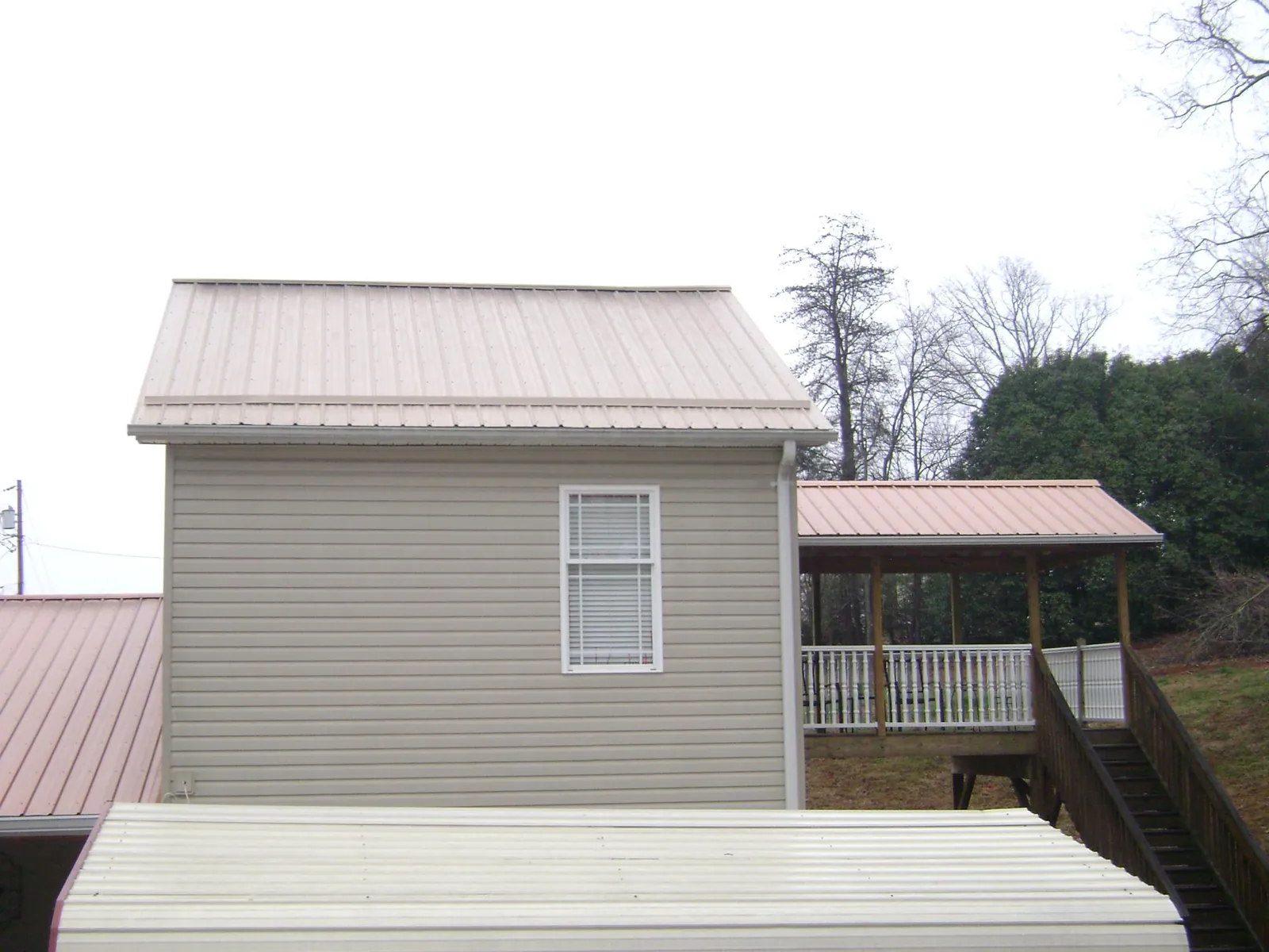 Tan metal roofs on a two story addition and attached porch, from a Roof Replacement job in Bear Creek